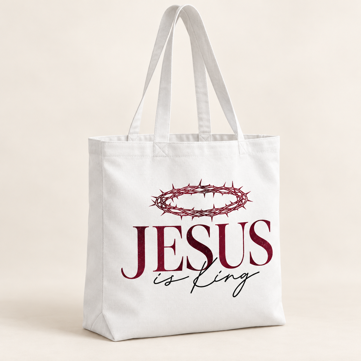White tote bag with long handles featuring a burgundy crown of thorns above burgundy JESUS lettering and black is King script