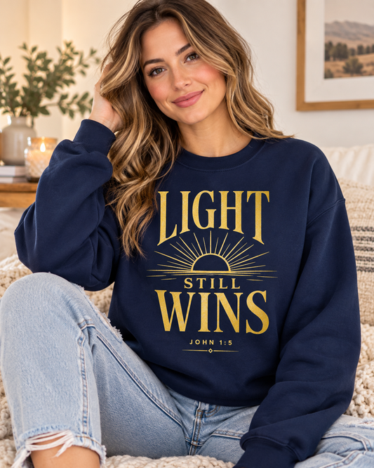 Navy blue Light Still Wins Christian sweatshirt featuring a gold sunrise design and John 1:5 from the Journey Wear collection.