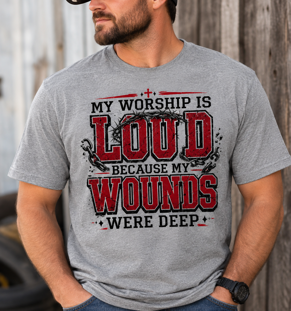 Man wearing a gray My Worship Is Loud Because My Wounds Were Deep Christian T-shirt with distressed red and black lettering, crown of thorns, broken chains, and cross details.