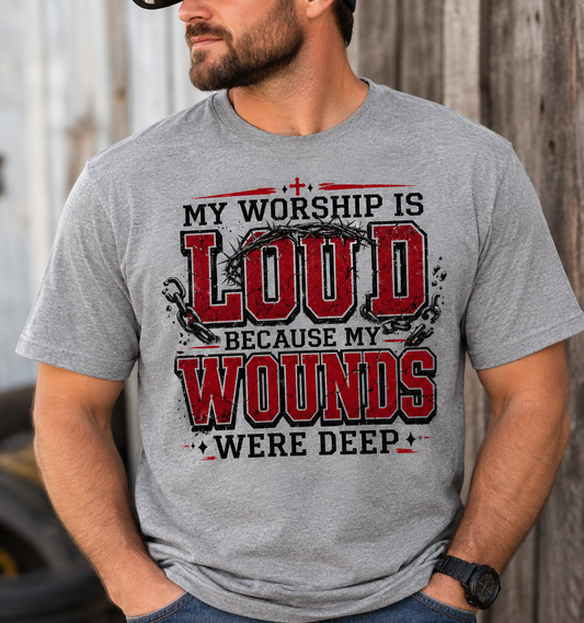 Man wearing a gray My Worship Is Loud Because My Wounds Were Deep Christian T-shirt with distressed red and black lettering, crown of thorns, broken chains, and cross details.