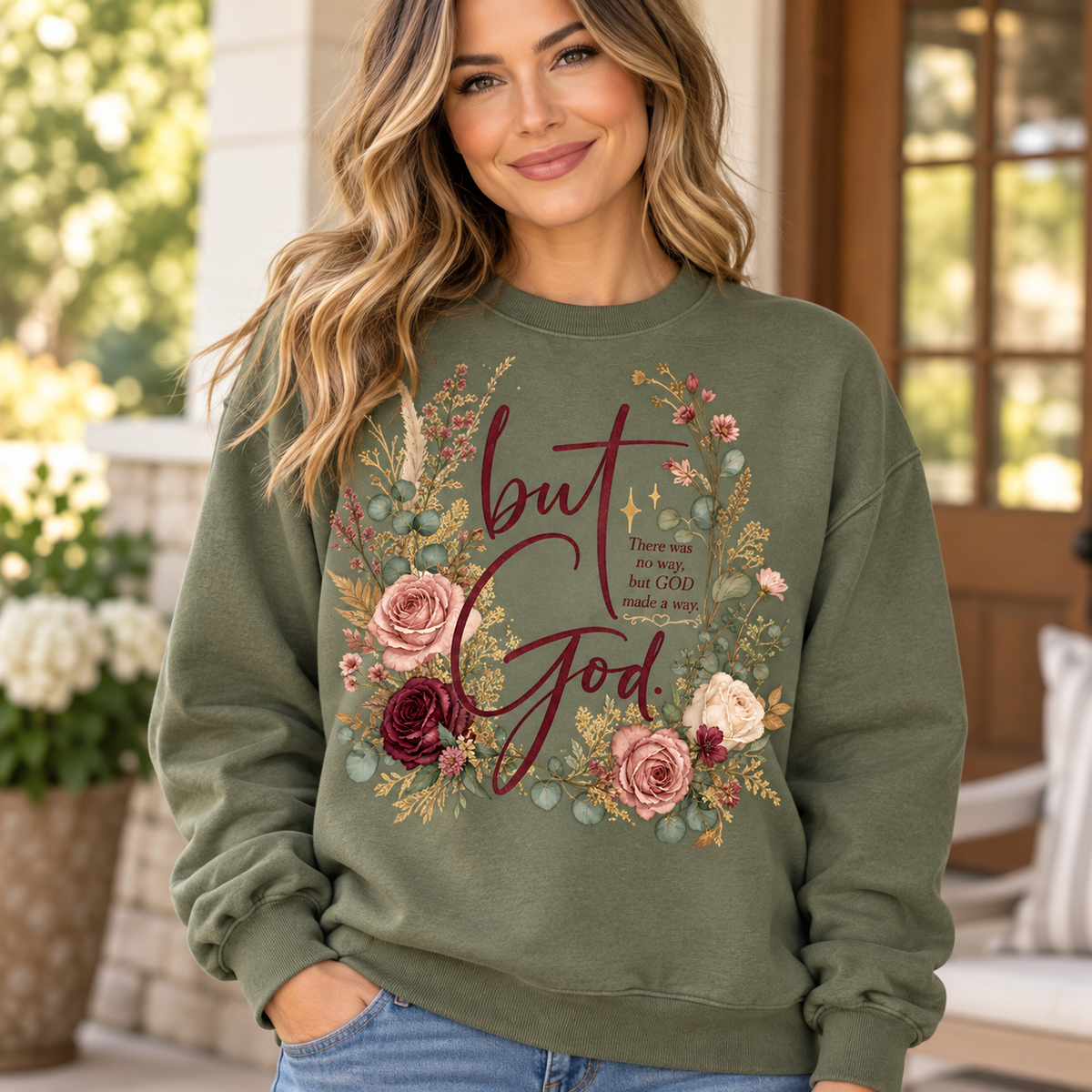 Woman wearing an olive green crewneck sweatshirt with burgundy But God lettering, blush and cream roses, sage greenery, and gold-colored botanical accents.