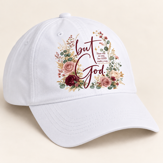 White ball cap with a curved brim and printed But God floral design featuring burgundy lettering, blush roses, cream flowers, and sage greenery.